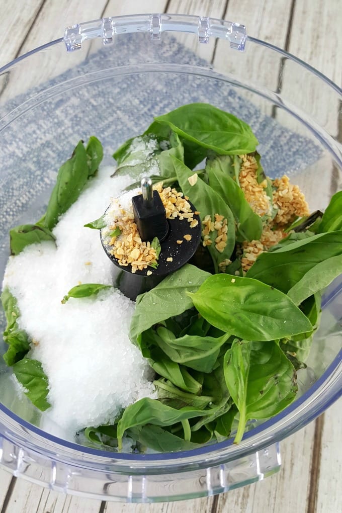A close up of a food processor with fresh basil, kosher salt and dried minced garlic to be made into basil salt.