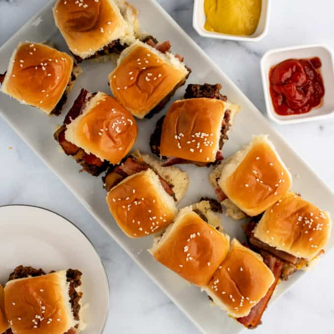 Top down view of bacon cheese sliders on a white platter.