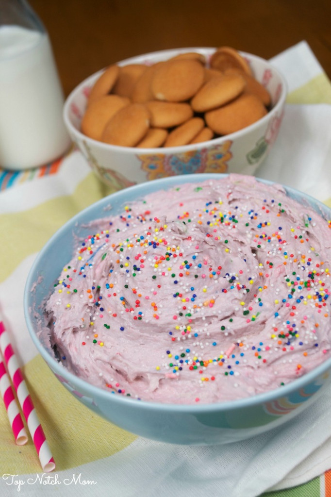 Pink cake batter dip with sprinkles in a blue bowl. Nilla wafer dippers in the back.