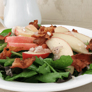 Close up image of an apple bacon spinach salad on a white plate.