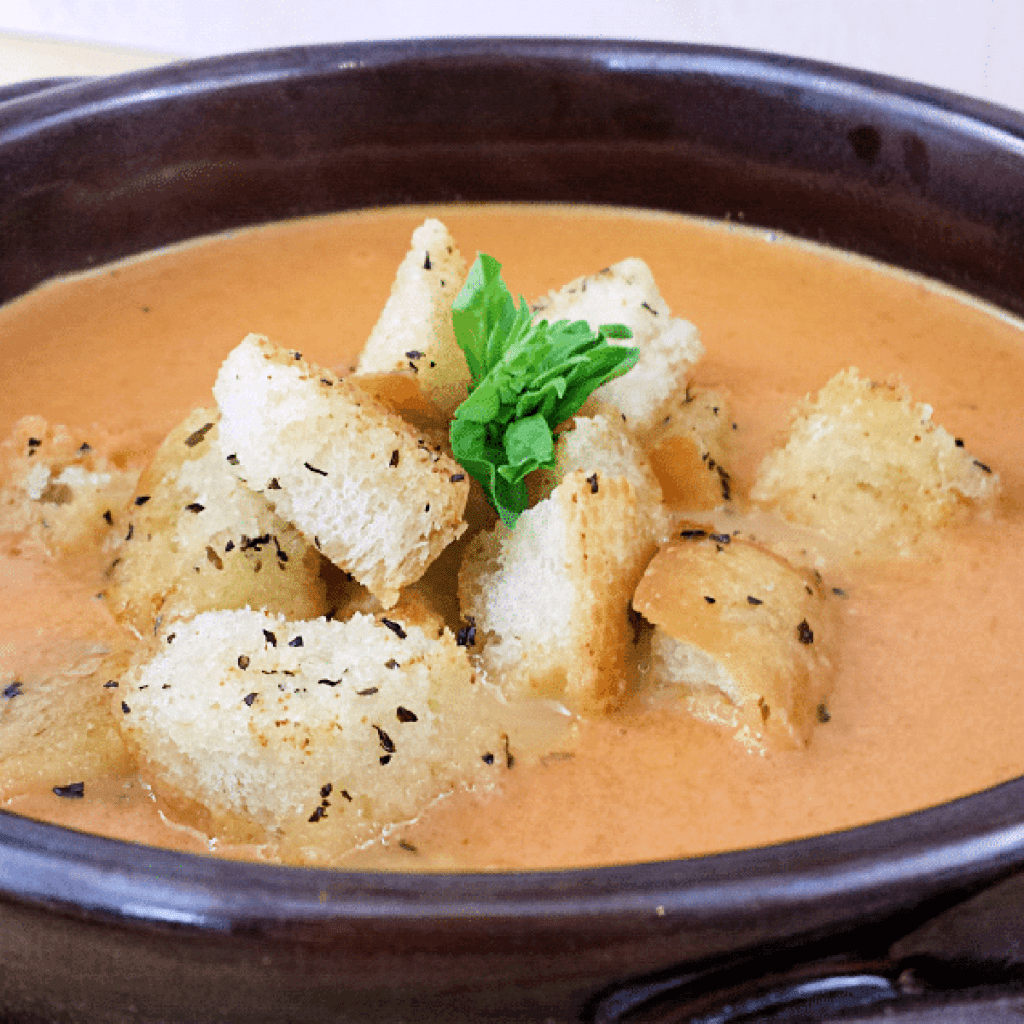 Close up of Creamy Tomato Basil Soup in a bowl with croutons on top.