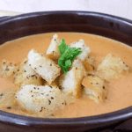 Close up image of creamy tomato basil soup in a brown bowl.