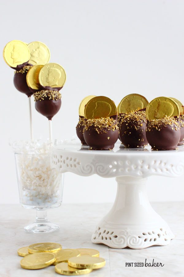 Gold cake pops on a white cake plate and in a parfait dish next to gold coin candies.