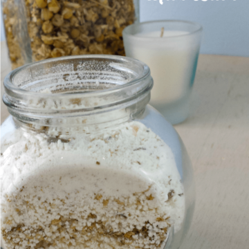 Chamomile milk bath in a glass jar with ingredients behind it.