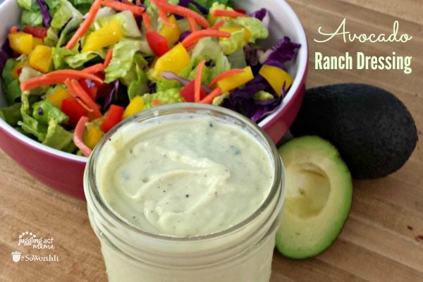 Top down view of avocado ranch dressing in a glass mason jar next to a sliced avocado and fresh salad greens.