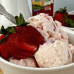 Close up image of strawberry ice cream in a white bowl, topped with fresh strawberries.