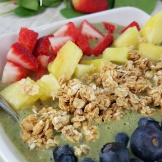 Close up image of a green smoothie bowl topped with fresh fruit and granola.
