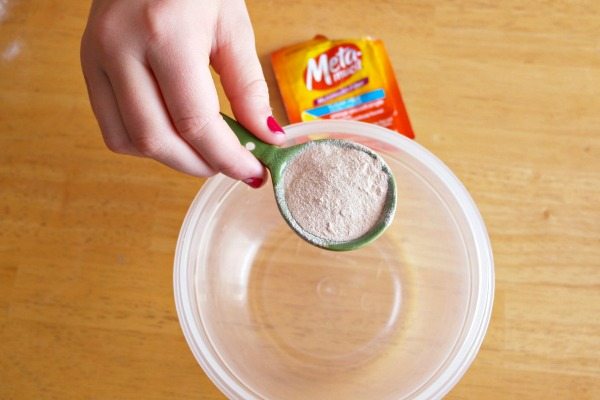 a woman's hand holds measuring spoon with ingredients to make homemade ooblek