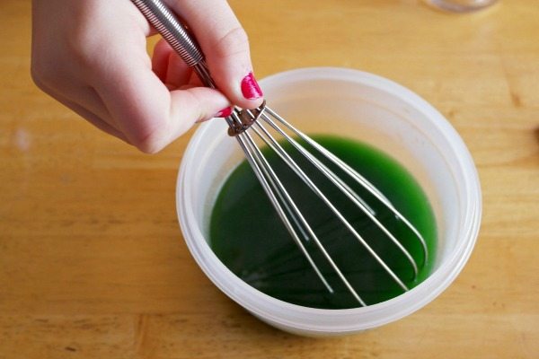 a woman's hand holds a whisk in a small bowl with green liquid