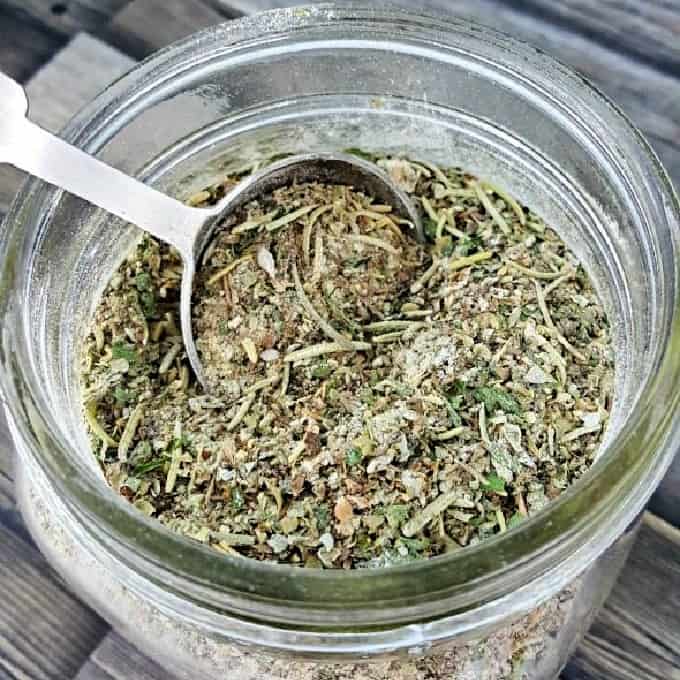 Glass jar and measuring spoon filled with homemade Italian seasoning.