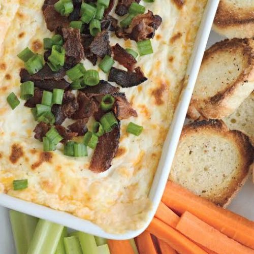 Cheesy Bacon Dip in white bowl with crackers for dipping.