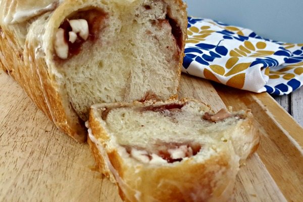 A loaf of Strawberry Cream Cheese Pull Apart Bread is shown on a cutting board. The top is drizzled with icing and the loaf is cut open showing pockets of cream cheese and strawberry jam.