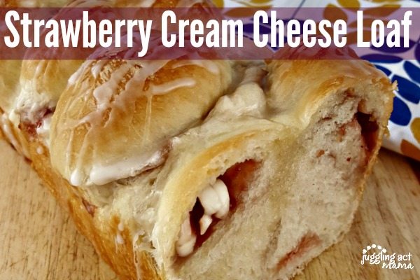 A loaf of Strawberry Cream Cheese Pull Apart Bread is shown on a cutting board. The top is drizzled with icing and the loaf is cut open showing pockets of cream cheese and strawberry jam.
