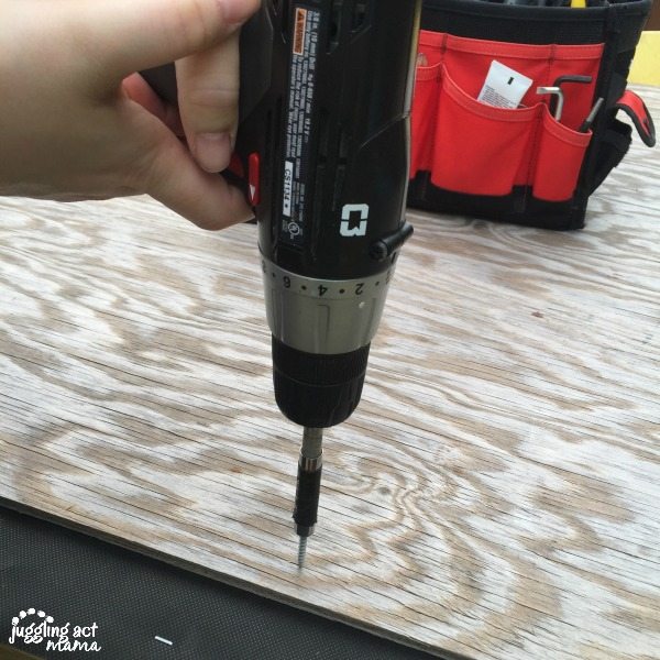 Drill drilling a screw into a plywood board.