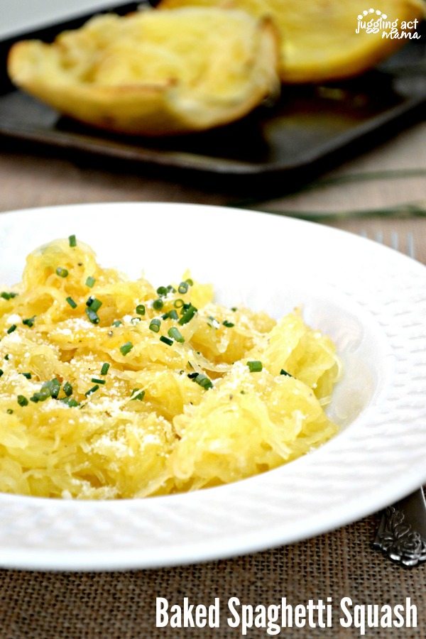 Baked spaghetti squash recipe garnished with Parmesan cheese and chives in a white pasta bowl. In the background is a sheet pan with baked spaghetti squash halves.