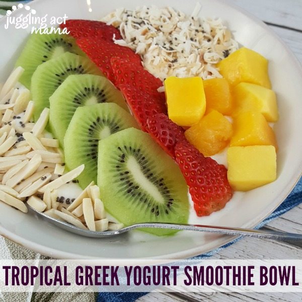 close up of a tropical smoothie bowl with greek yogurt, slivered almonds, slices of kiwi and strawberries, chunks of mango and toasted coconut with chia seeds.