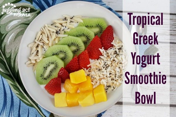 close up of a tropical smoothie bowl with greek yogurt, slivered almonds, slices of kiwi and strawberries, chunks of mango and toasted coconut with chia seeds.