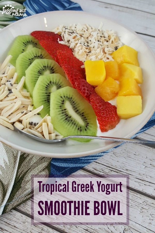 close up of a tropical smoothie bowl with greek yogurt, slivered almonds, slices of kiwi and strawberries, chunks of mango and toasted coconut with chia seeds.