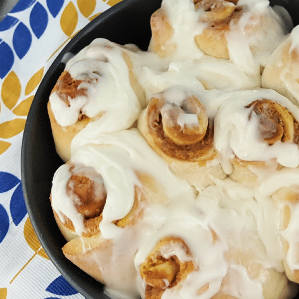 Pan of Pumpkin Cinnamon Rolls with cream cheese icing.,