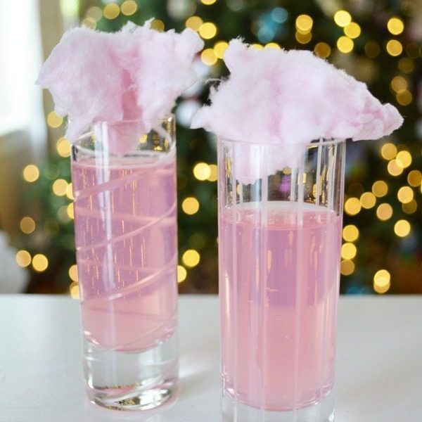 Two tall thin classes of cotton candy mocktail drinks with cotton cacdy on top.