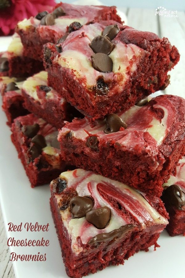 A close up of red velvet cheesecake brownies with chocolate chips stacked on a white plate.