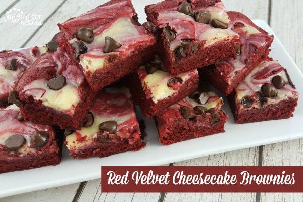 Red velvet cheesecake brownies with chocolate chips stacked high on a white plate on a white wood table. 