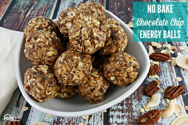 A white bowl filled with Oatmeal Peanut Butter Chocolate Chip Balls sitting on a wooden surface. Pecans and toasted coconut is sprinkled around.
