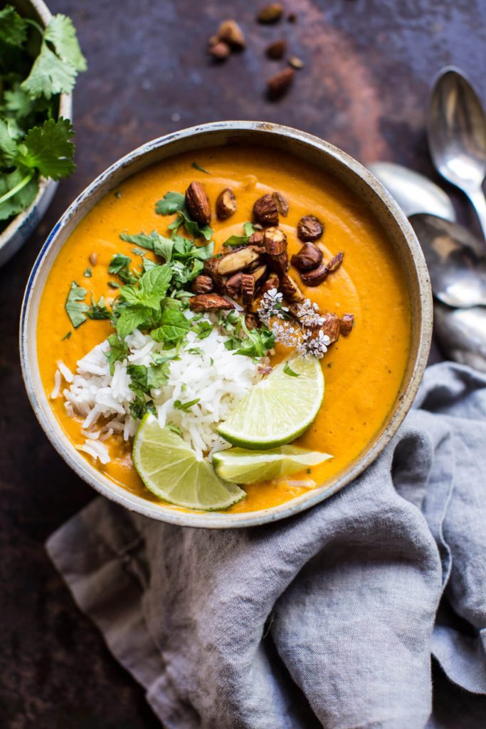 Thai Carrot Sweet Potato Soup in a bowl with rice and lime wedges.