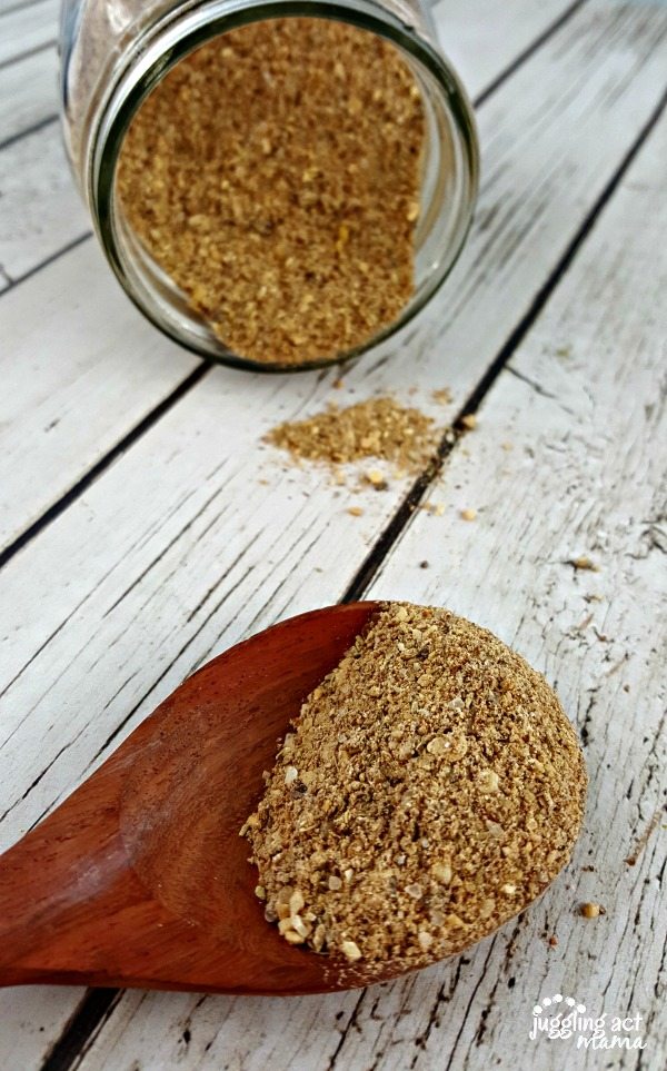 Homemade Montreal Seasoning Mix spilling from a mason jar behind a wooden spoon with a scoop of seasoning.
