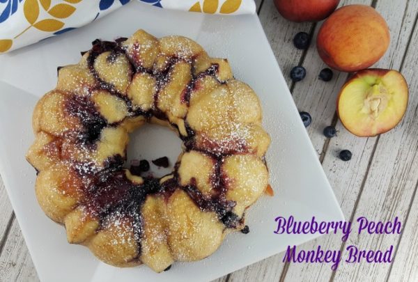 Blueberry Monkey Bread on a platter with fresh peaches and blueberries.