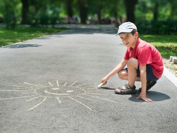 Child drawing sun on asphalt in a park