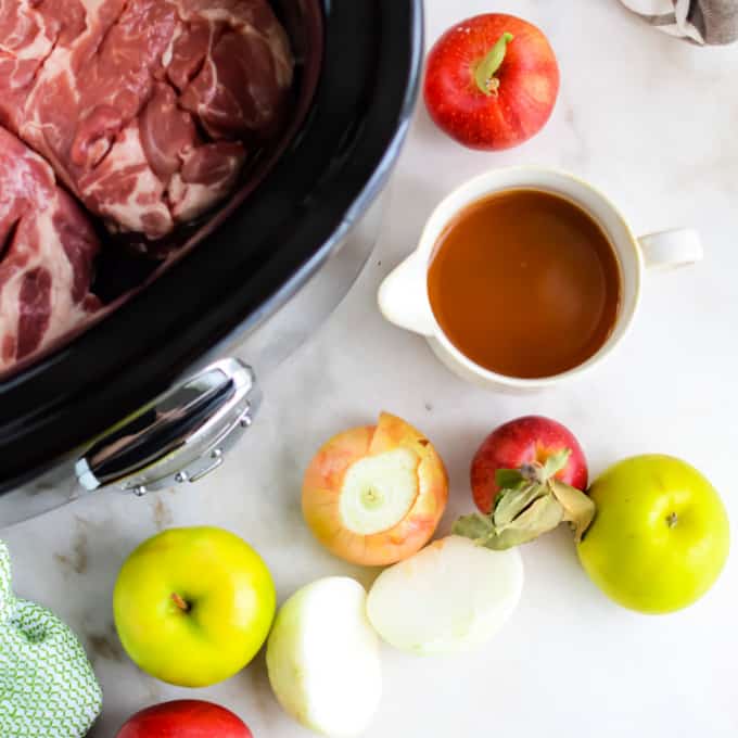 Ingredients to make slow cooker roast pork on the counter surrounding a slow cooker.