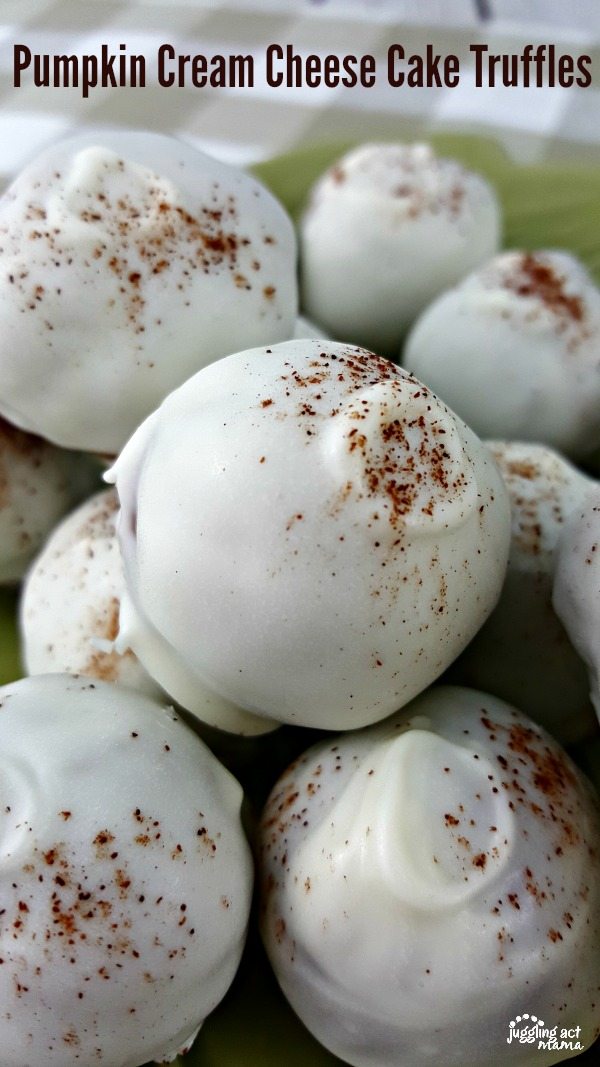 Pumpkin Cake Balls covered in white chocolate and sprinkled with cinnamon sit on a green leaf shaped plate on top of a tan and white checkered cloth. 