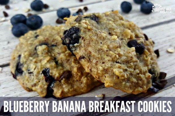 Two blueberry breakfast cookies sitting on a rustic wood surface, surrounded by fresh blueberries. 