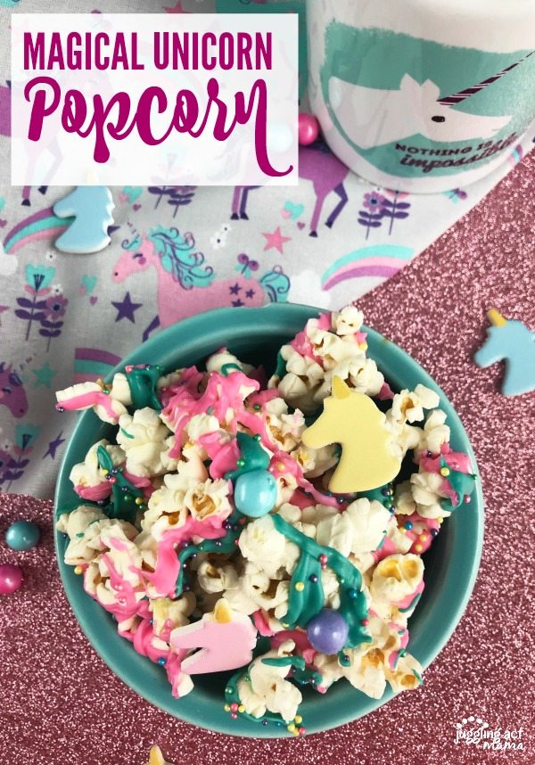 Magical Unicorn Popcorn with colored chocolate, unicorn shapes, sixlet candies and sprinkles in a teal bowl on top of a glittery pink surface with a pink and purple unicorn print napkin.