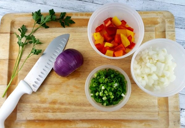 Top down view of a cutting board with containers of chopped onions, peppers and scallions.