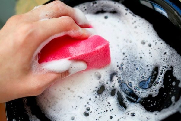 hands with sponge washing dishes in kitchen sink
