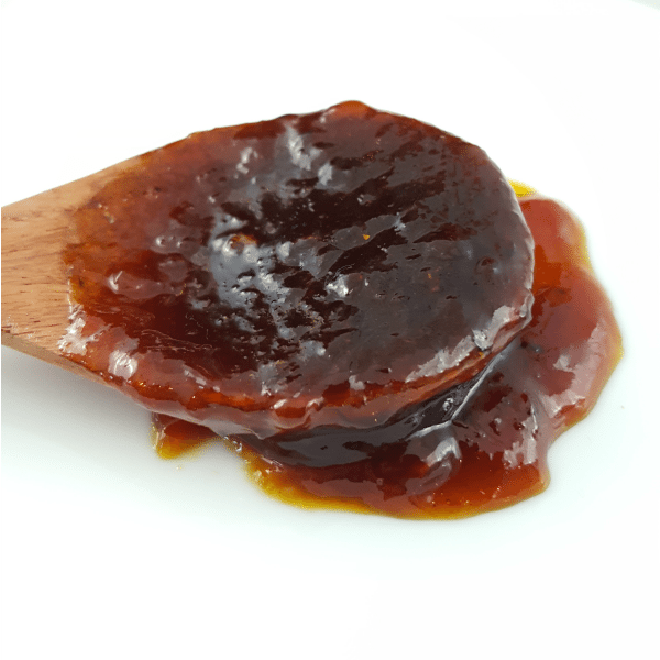 A wooden spoon covered in Pineapple Bourbon BBQ Sauce on a white surface.