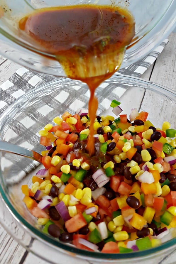 Cumin and chili powder dressing pouring onto cowboy caviar ingredients in a bowl.