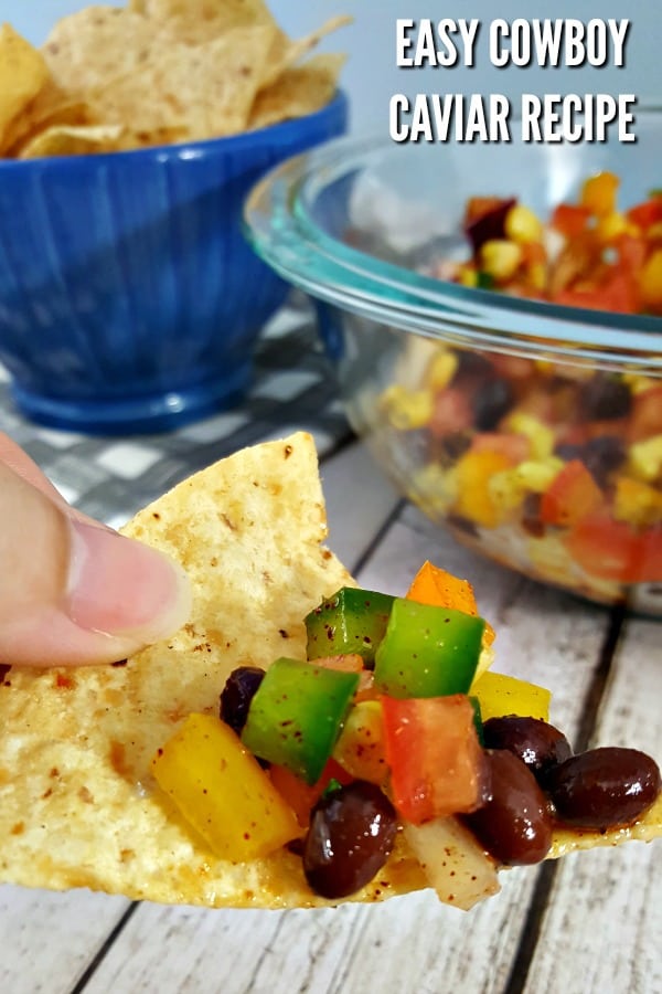 Fingers holding a tortilla chip with cowboy caviar on top.