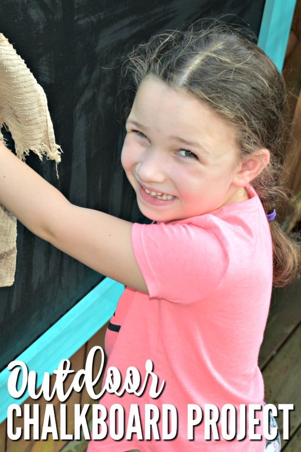 Smiling Girl wiping an Outdoor Chalkboard with a cloth.