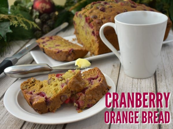 A mug next to two slices of Orange Cranberry Bread on a little plate with a butter knife.