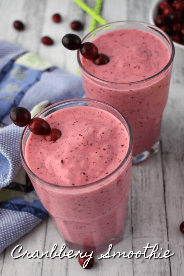 Two pineapple cranberry smoothies on a wooden table next to a blue hand towel.