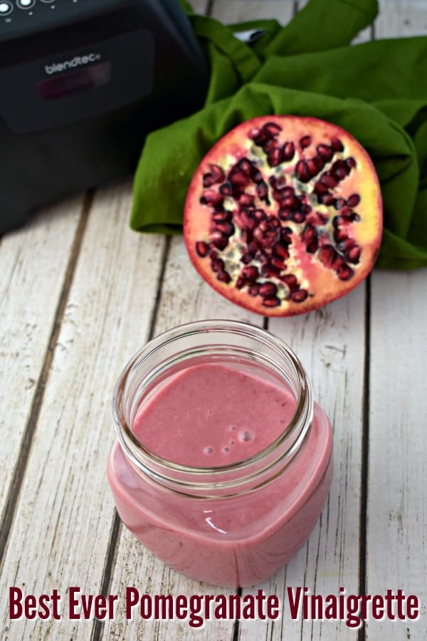 Jar of pomegranate dressing with half of a pomegranate in the background.