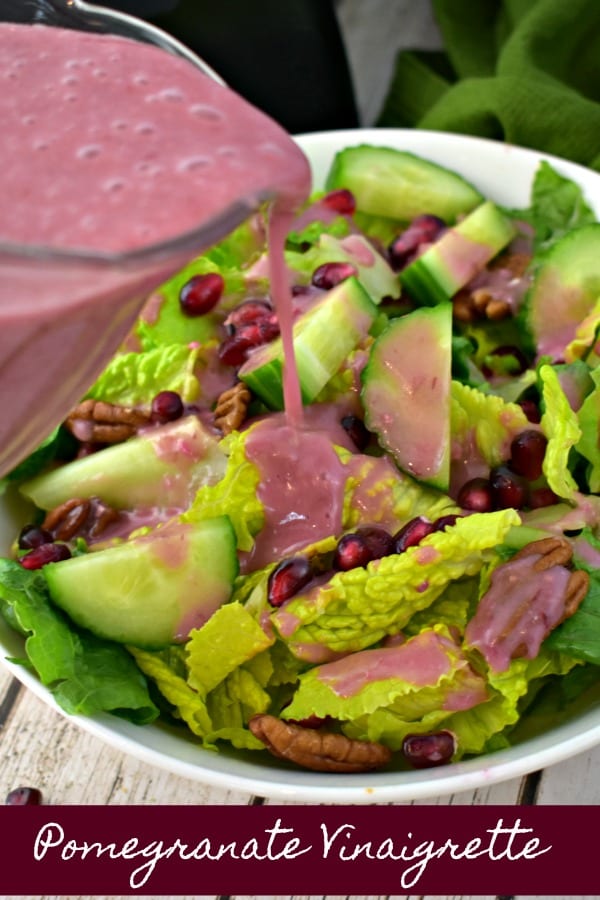 close up of pitcher pouring pomegranate dressing onto a bowl of salad