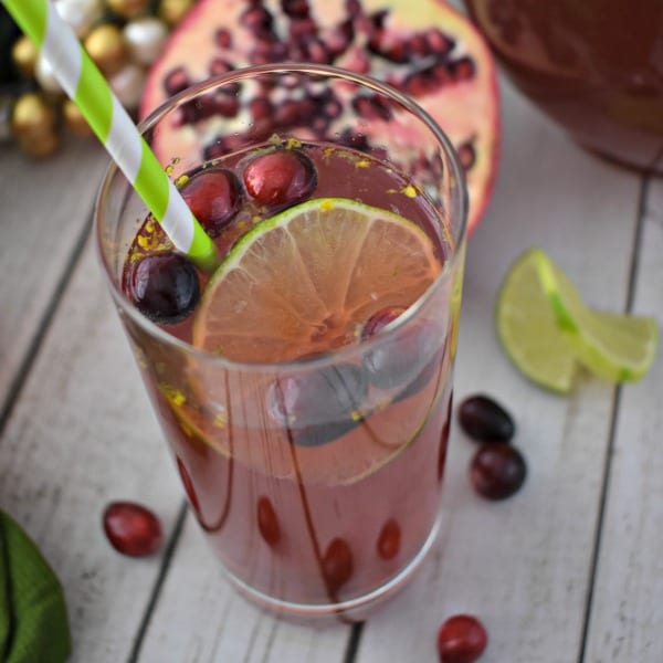 close up of a class of pomegranate holiday punch garnished with a lime wheel and fresh cranberries.