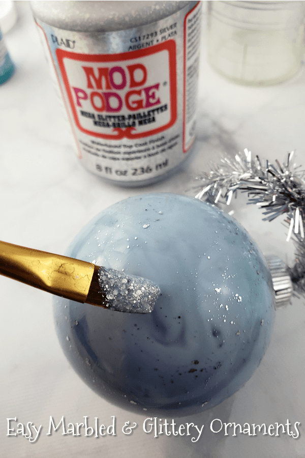 Close up image of a gray marble Christmas ornament being covered with glitter paint. 