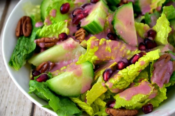 Close up of a bowl of salad with cucumbers, pomegranate seeds and pomegranate dressing.