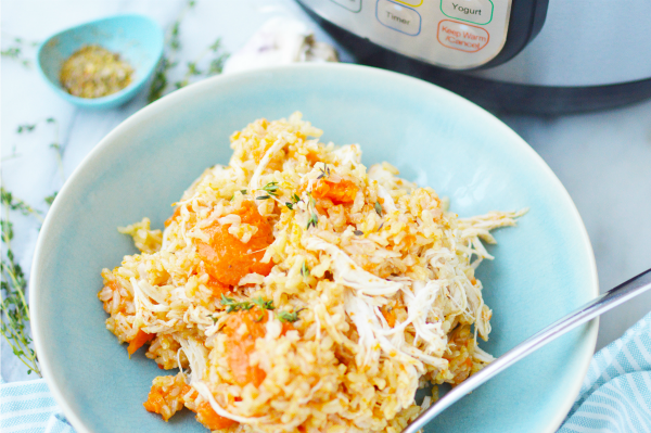 Instant Pot chicken and rice recipe- a blue bowl with brown rice, shredded chicken and sliced carrots next to an Instant Pot