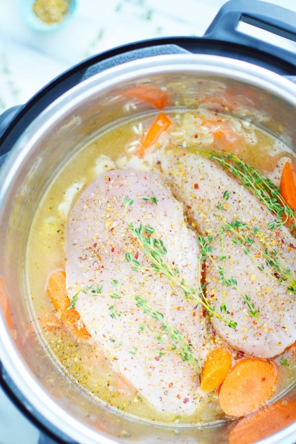 Two chicken breasts in an instant pot with rice, carrots and chicken stock